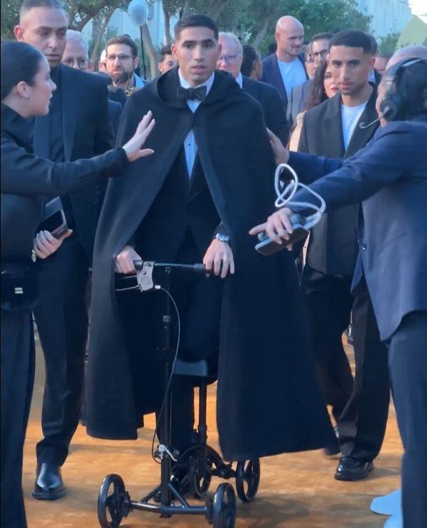 喜感拉满阿什拉夫穿戴黑披风推着助行器，蹦蹦跳跳拍照领奖